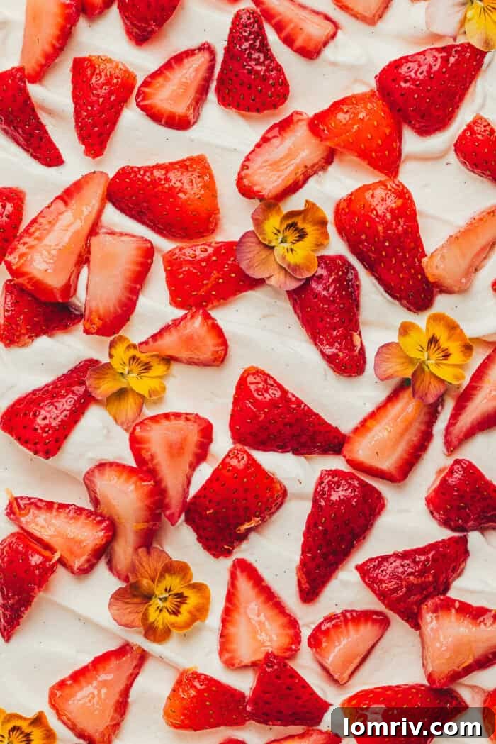 The decorated top of a strawberry tres leches cake, garnished with whole fresh strawberries and edible flowers.