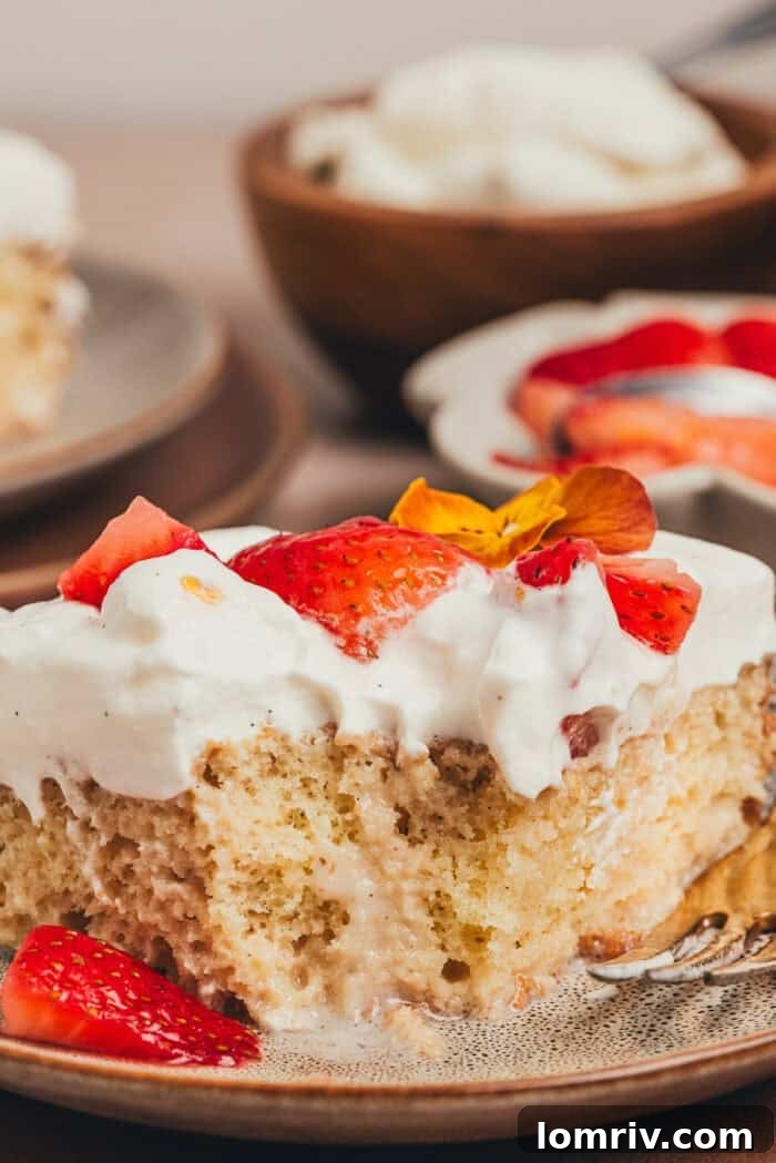 A close-up of a slice of strawberry tres leches cake, showing the fork taking a bite, emphasizing its delicious texture.