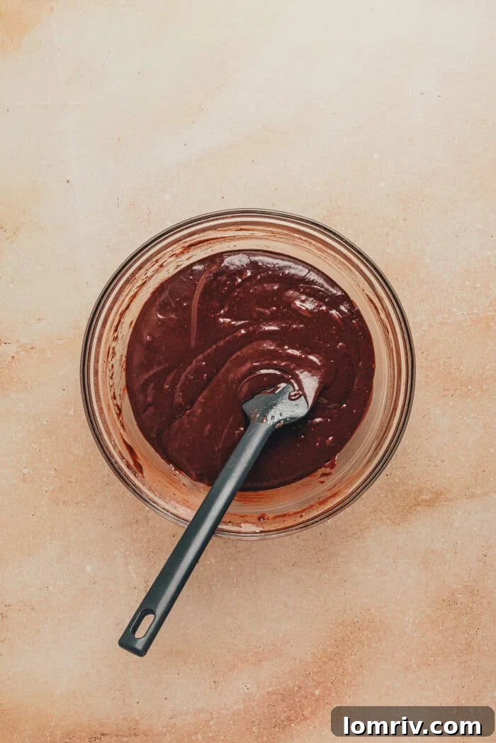 The final smooth and glossy chocolate cupcake batter in a glass bowl.