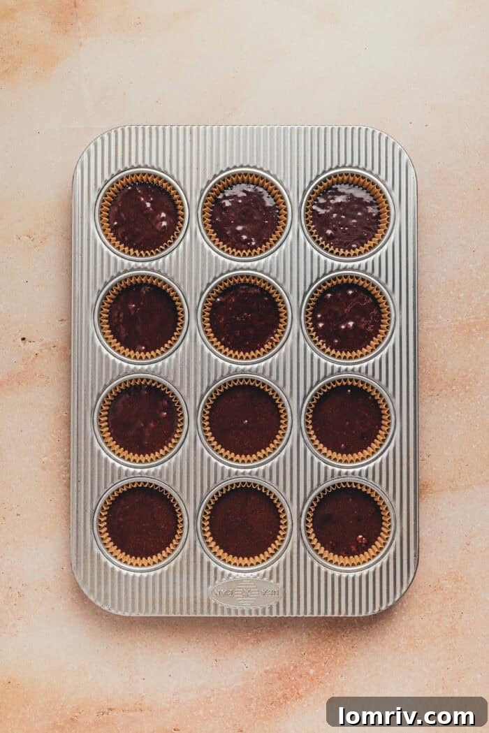 Cupcake batter being portioned into a lined muffin tin.
