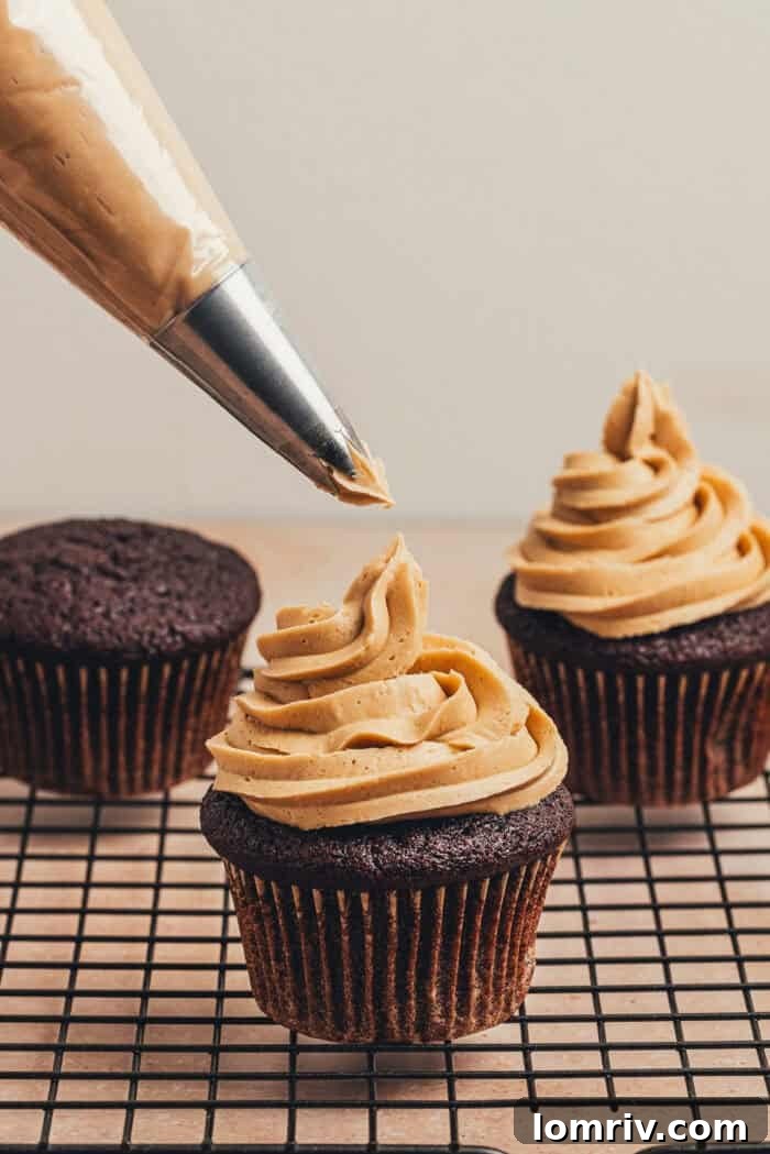 Piping the espresso frosting onto the cooled chocolate cupcakes using a piping bag and star tip.