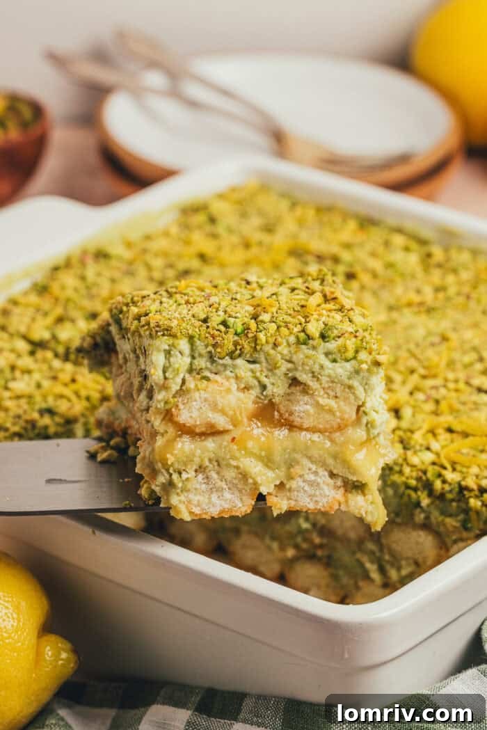 A slice of pistachio tiramisu cake being lifted out of the cake pan.