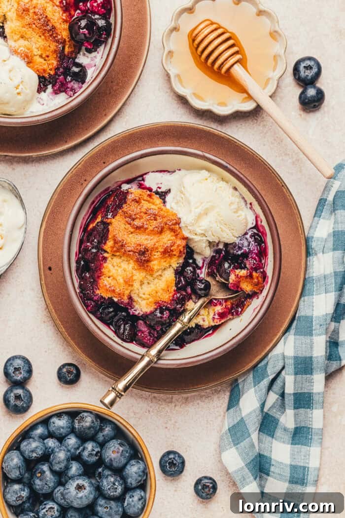 Honey-Sweetened Blueberry Cobbler Recipe with Fresh Berries 7 A bowl with a serving of blueberry cobbler and a spoon with various bowls of ingredients.